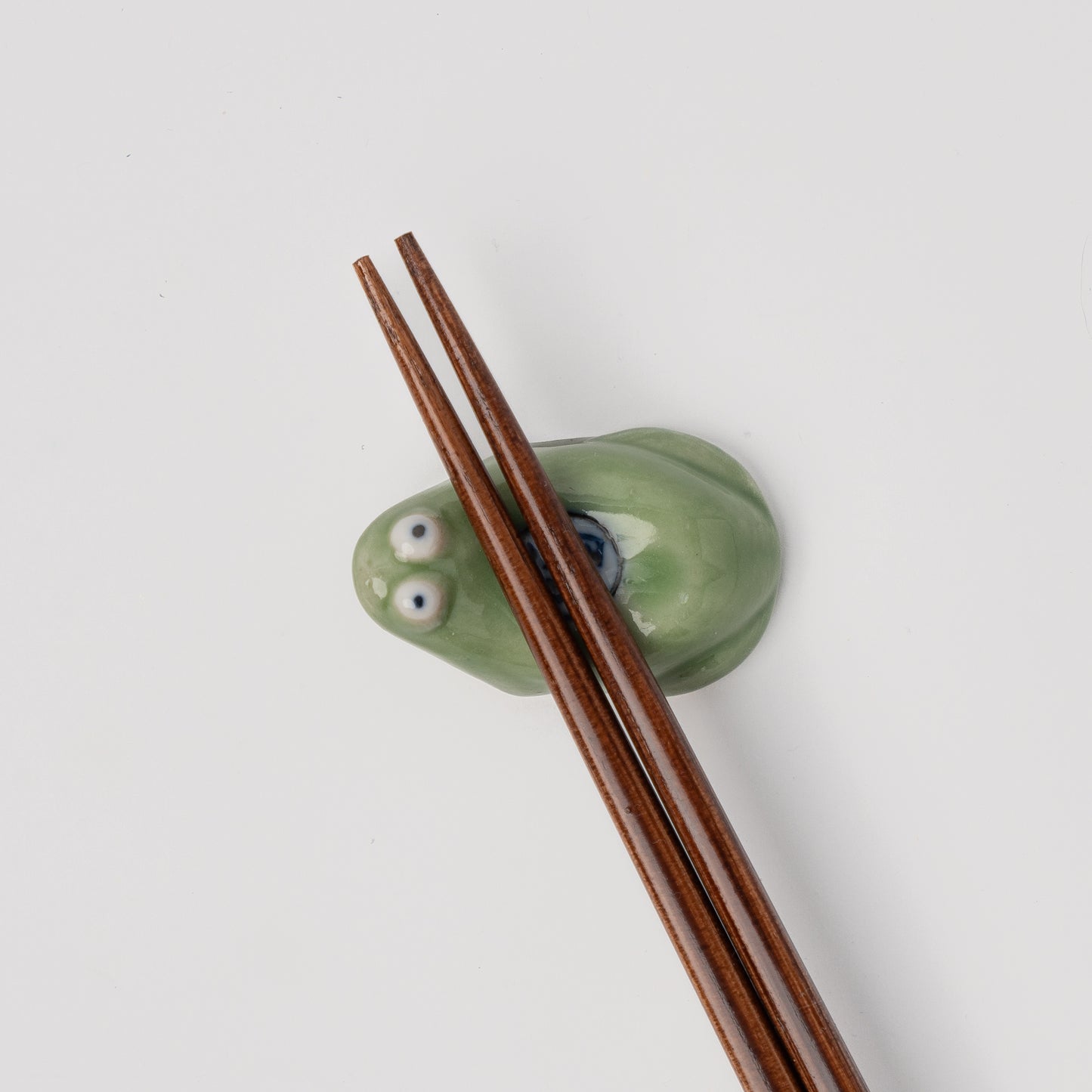 Green ceramic holder with googly eyes holding wooden chopsticks on a white background