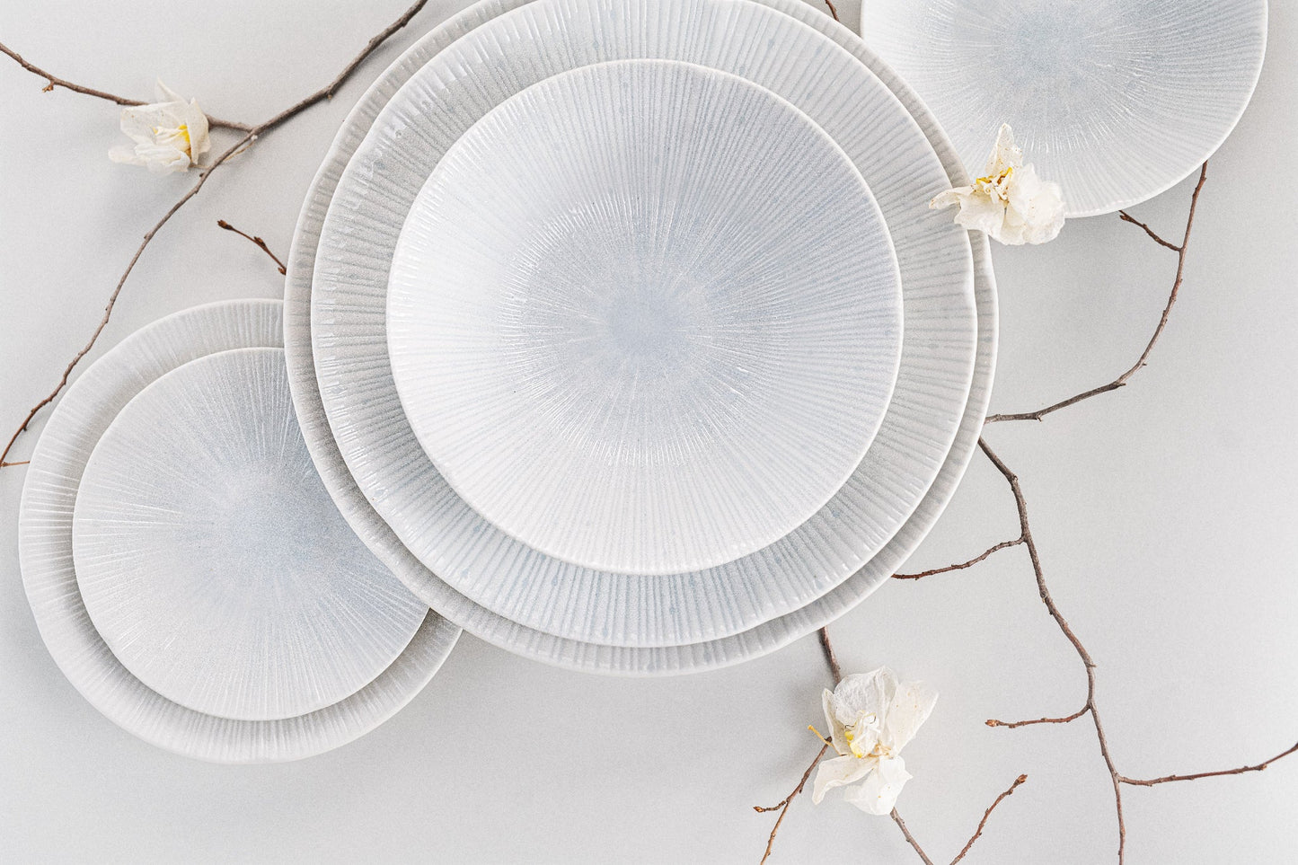 Set of white ceramic plates with a textured design on a light background with decorative branches.