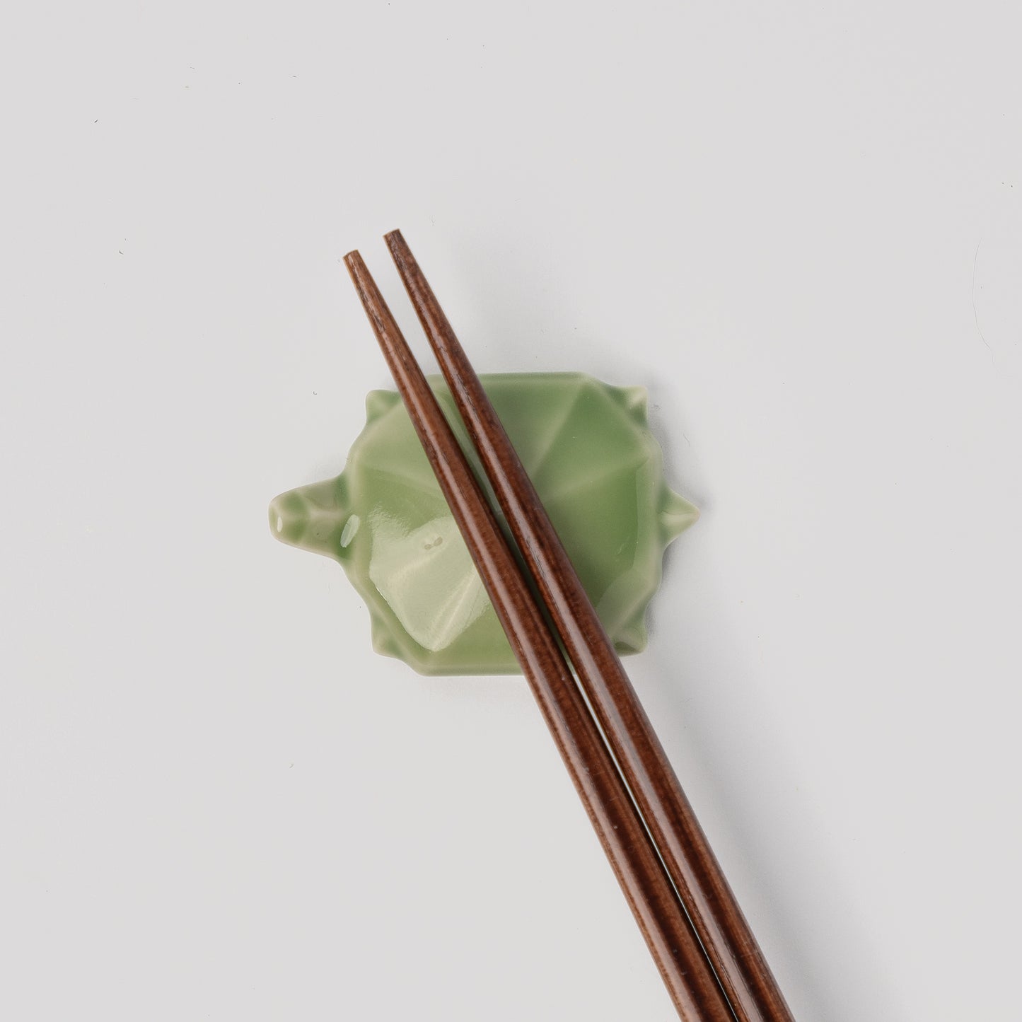 Wooden chopsticks on a green ceramic holder against a light gray background