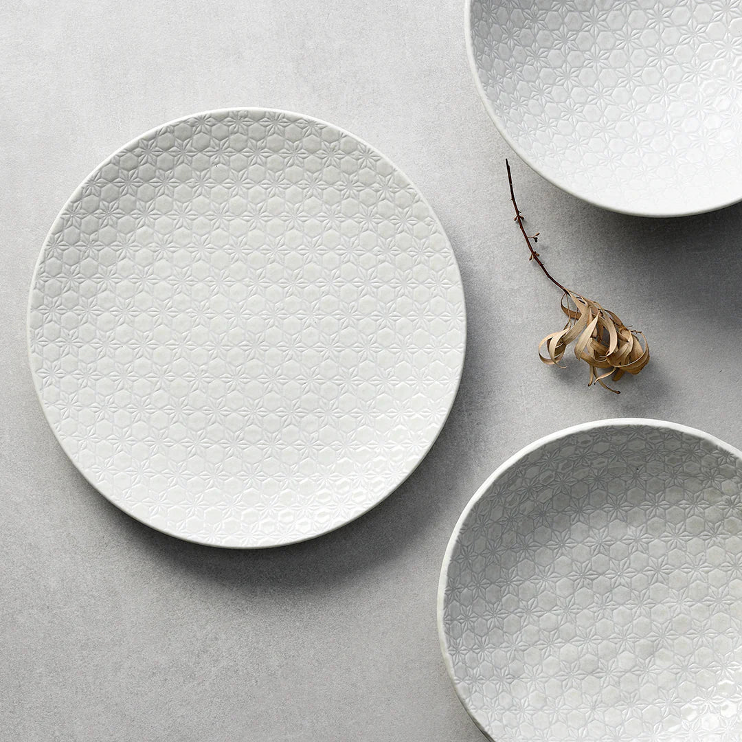 Three textured ceramic plates on a light gray surface with a dried plant.