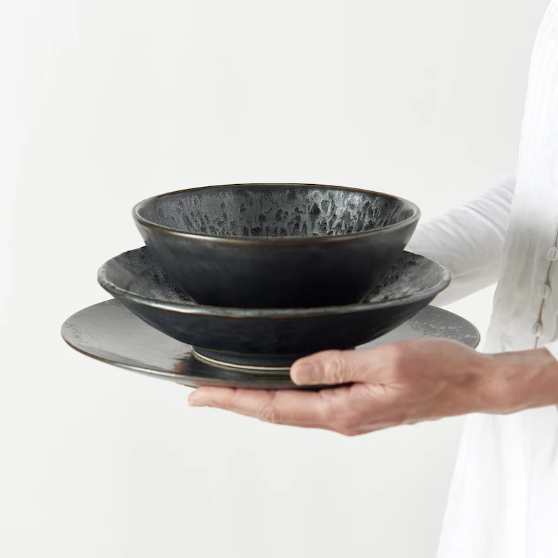 Person holding two black ceramic bowls on a white background