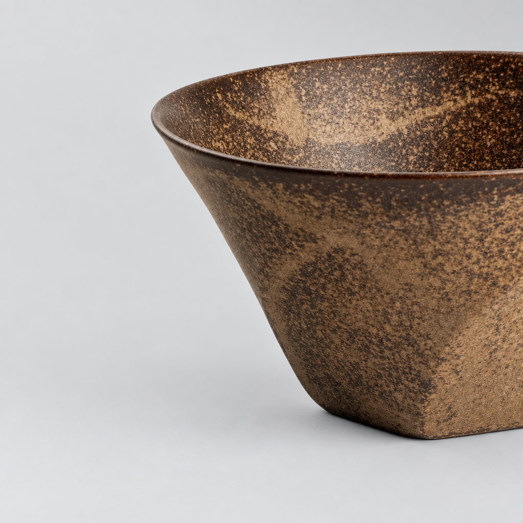 A close-up of a ceramic bowl with a textured, speckled brown and beige glaze, shown on a clean white background.