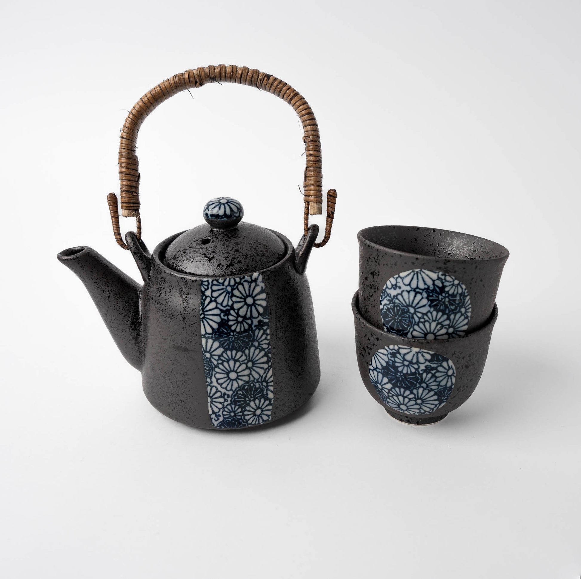 Black ceramic teapot with wicker handle and matching cups on a white background