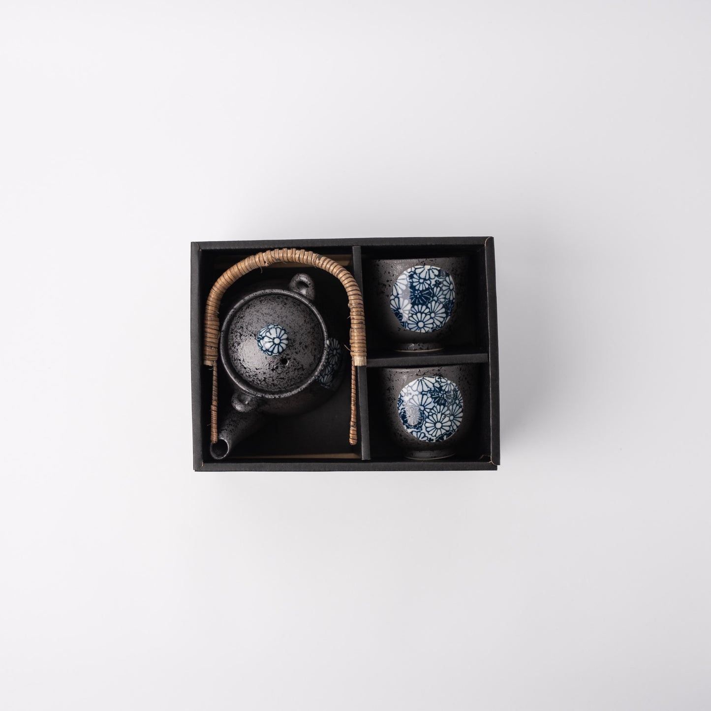 Ceramic tea set with two cups and a teapot in a black box on a light gray background