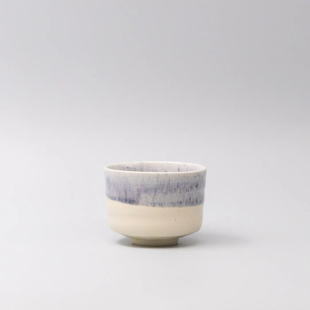 Small ceramic cup with a blue rim on a light gray background