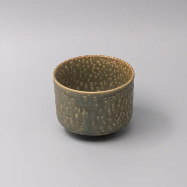 Small ceramic cup with textured surface on a gray background