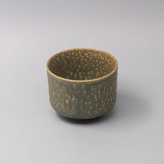 Small ceramic cup with textured surface on a gray background