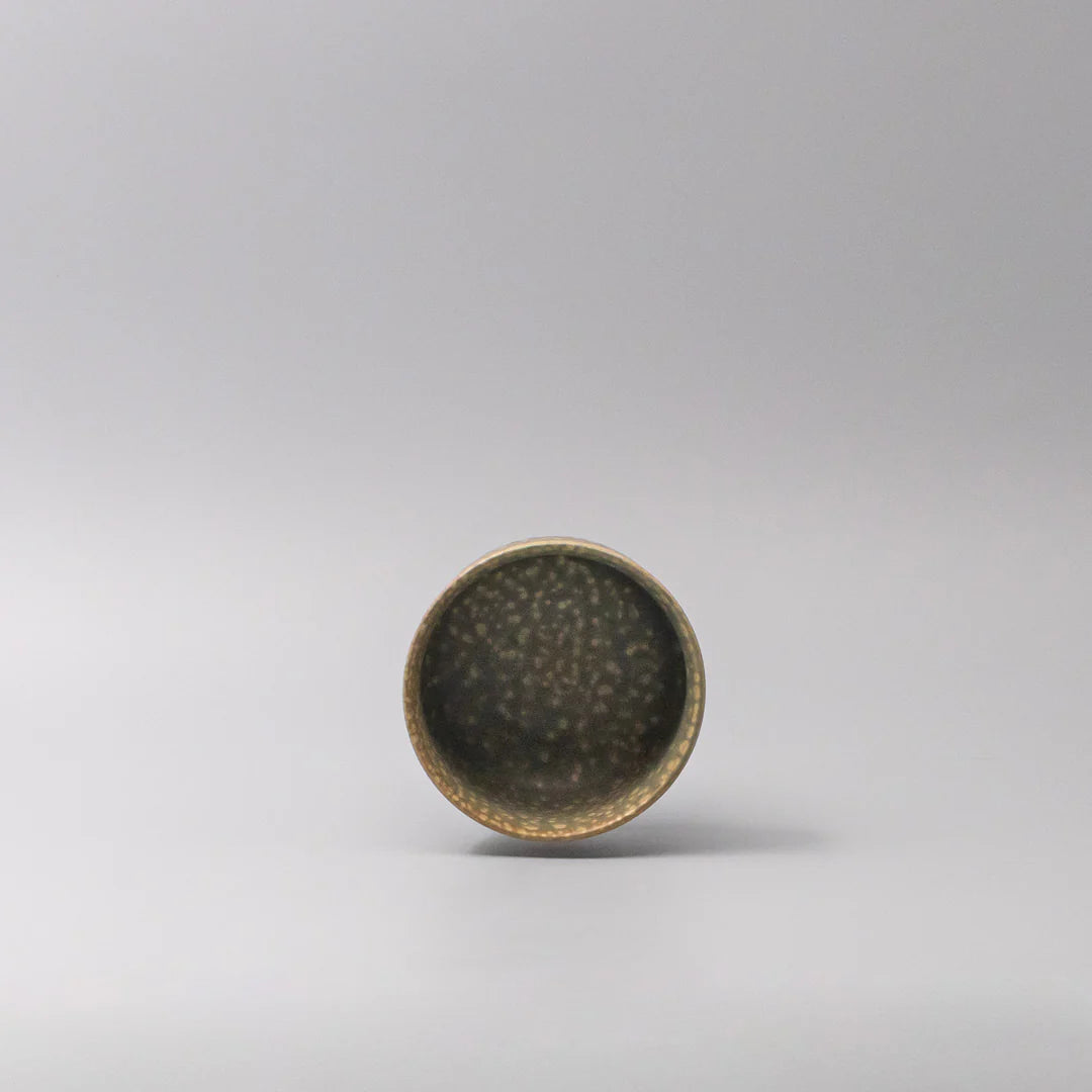 Small ceramic cup with speckled glaze on a light gray background
