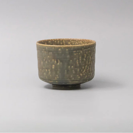 Small ceramic cup with textured surface on a light gray background