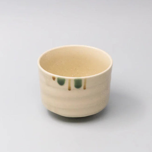 Small beige ceramic cup with green accents on a light gray background