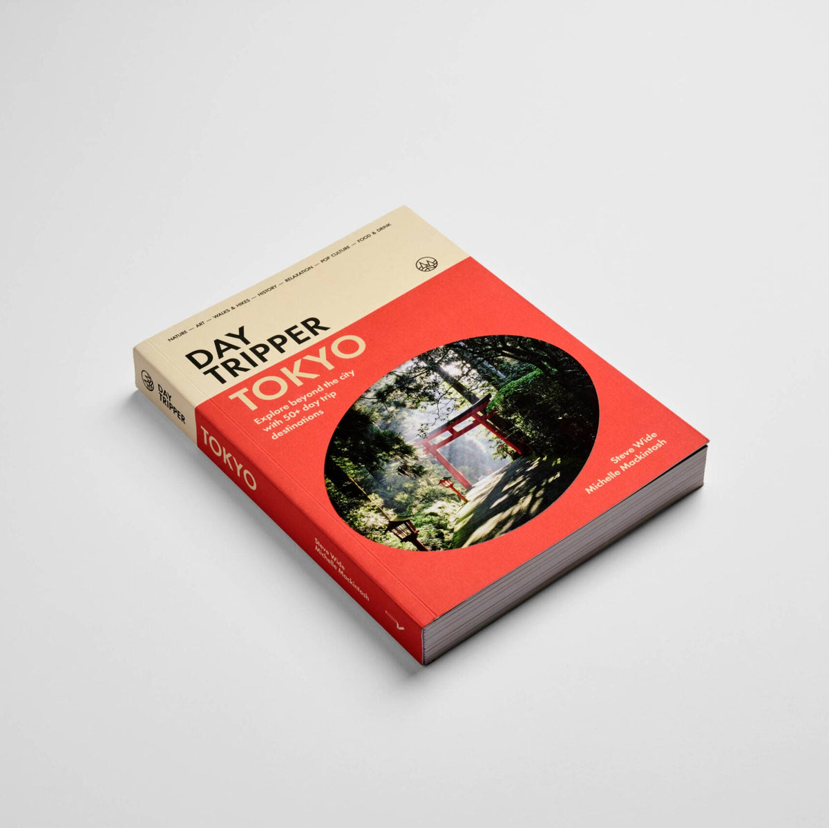 A travel guide book titled 'Day Tripper Tokyo' on a light gray background. The book cover features a bold red lower section with a circular scenic photograph of a Japanese torii gate in a forest, and a beige upper section with black and white text.