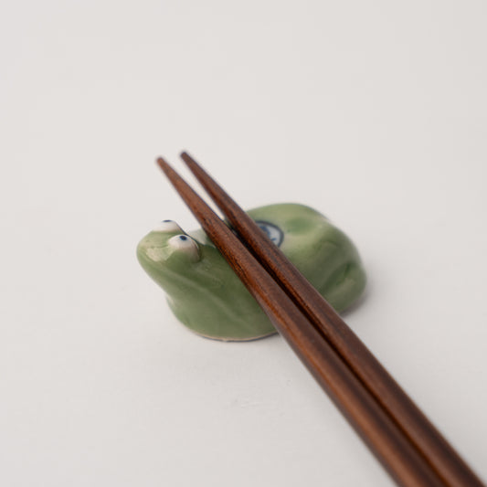 Frog-shaped chopstick rest with wooden chopsticks on a white background