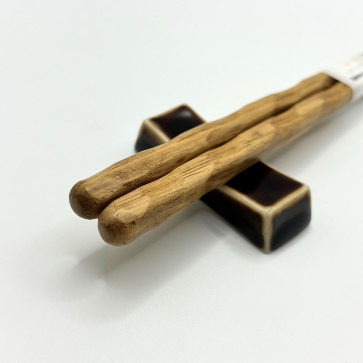 Two light brown wooden chopsticks resting on a dark ceramic chopstick holder against a clean white background.