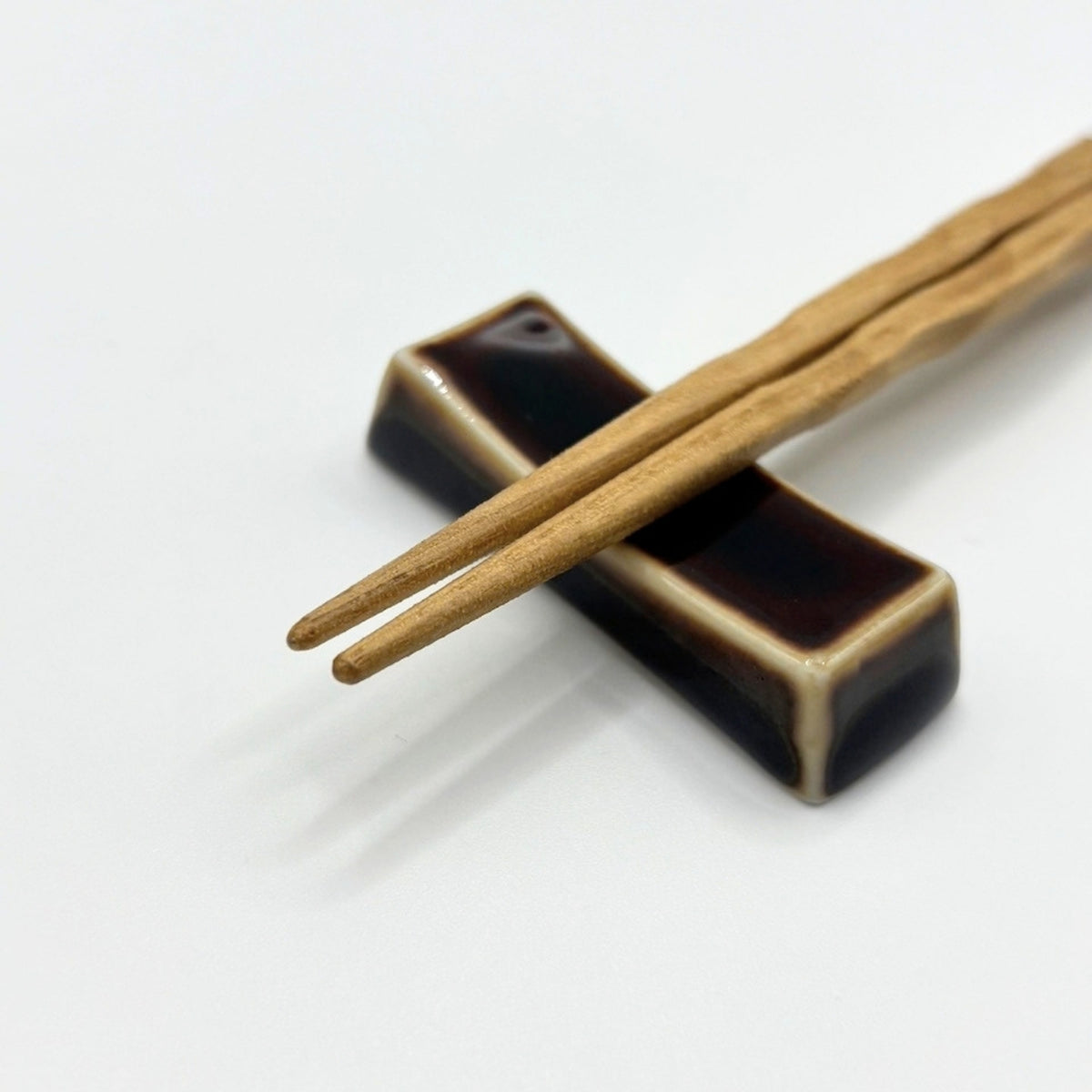 A pair of light brown wooden chopsticks resting on a glossy black ceramic chopstick holder with cream-colored edging, set against a clean white background.