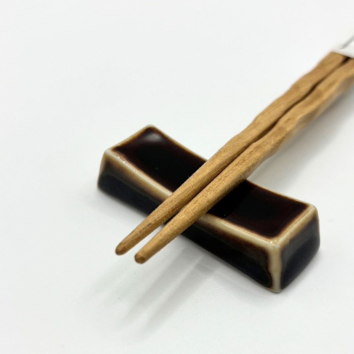 A pair of light brown wooden chopsticks resting on a dark brown and beige ceramic chopstick holder against a plain white background.