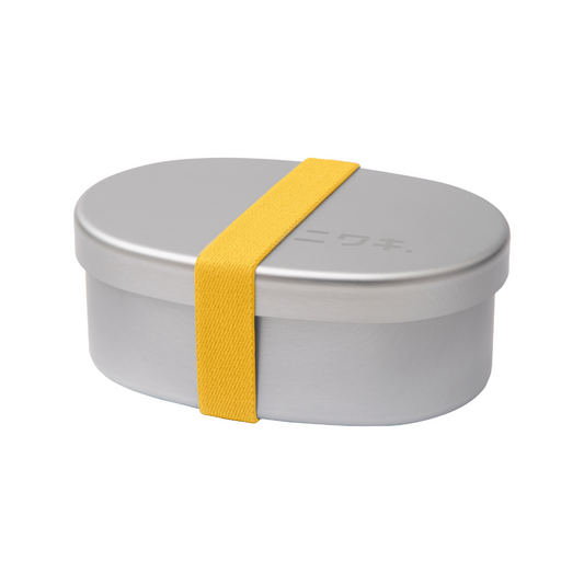 An oval-shaped Niwaki Bento Box with a gray aluminum exterior and a yellow elastic strap, closed with a plastic lid.