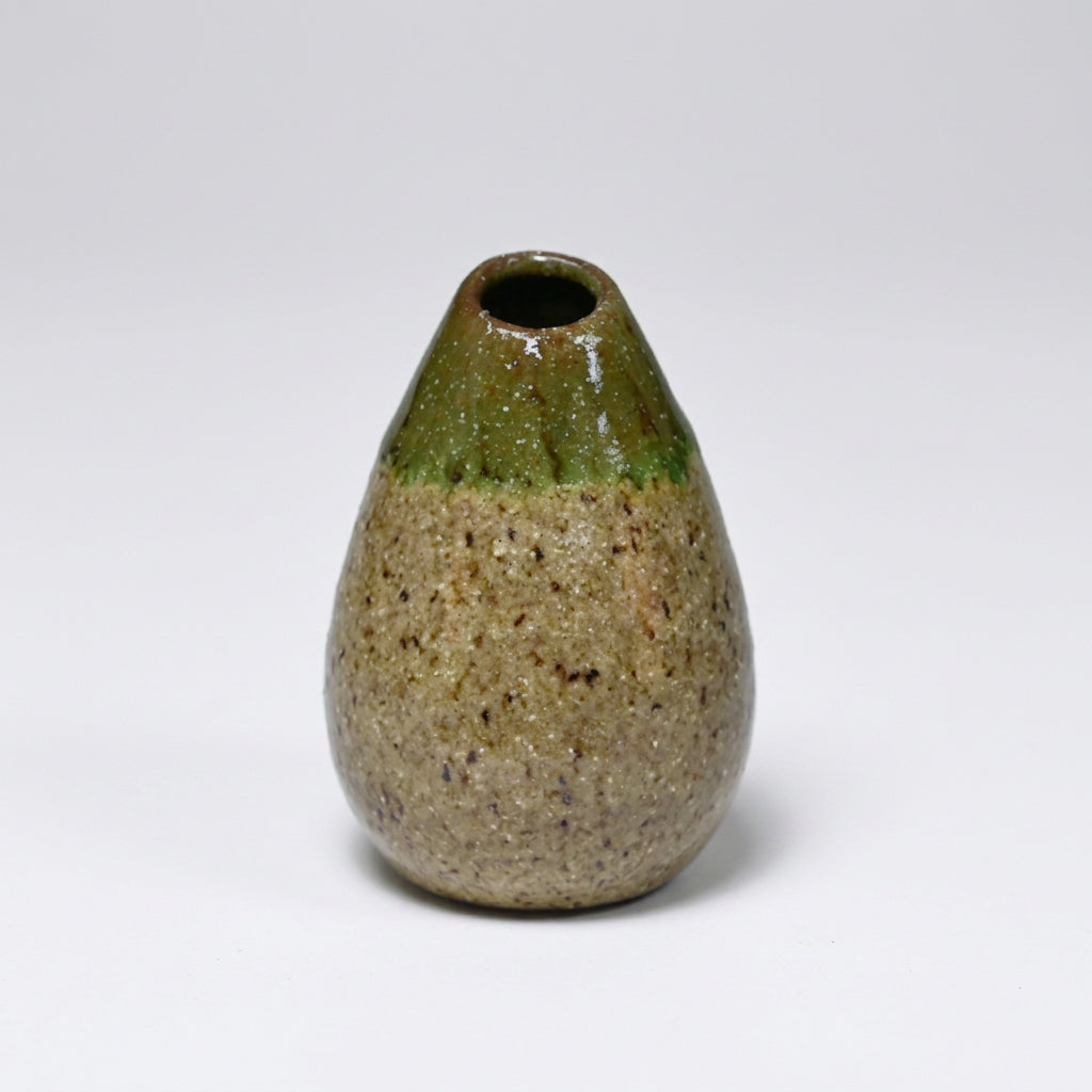 A small handmade ceramic vase with a teardrop shape, featuring a speckled beige and brown glaze on the lower body and a glossy dark green glazed top, set against a plain white background.