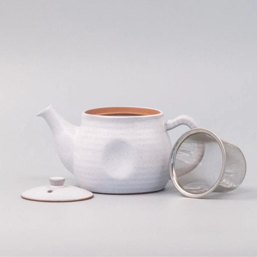 White ceramic teapot with a mesh filter on a light gray background