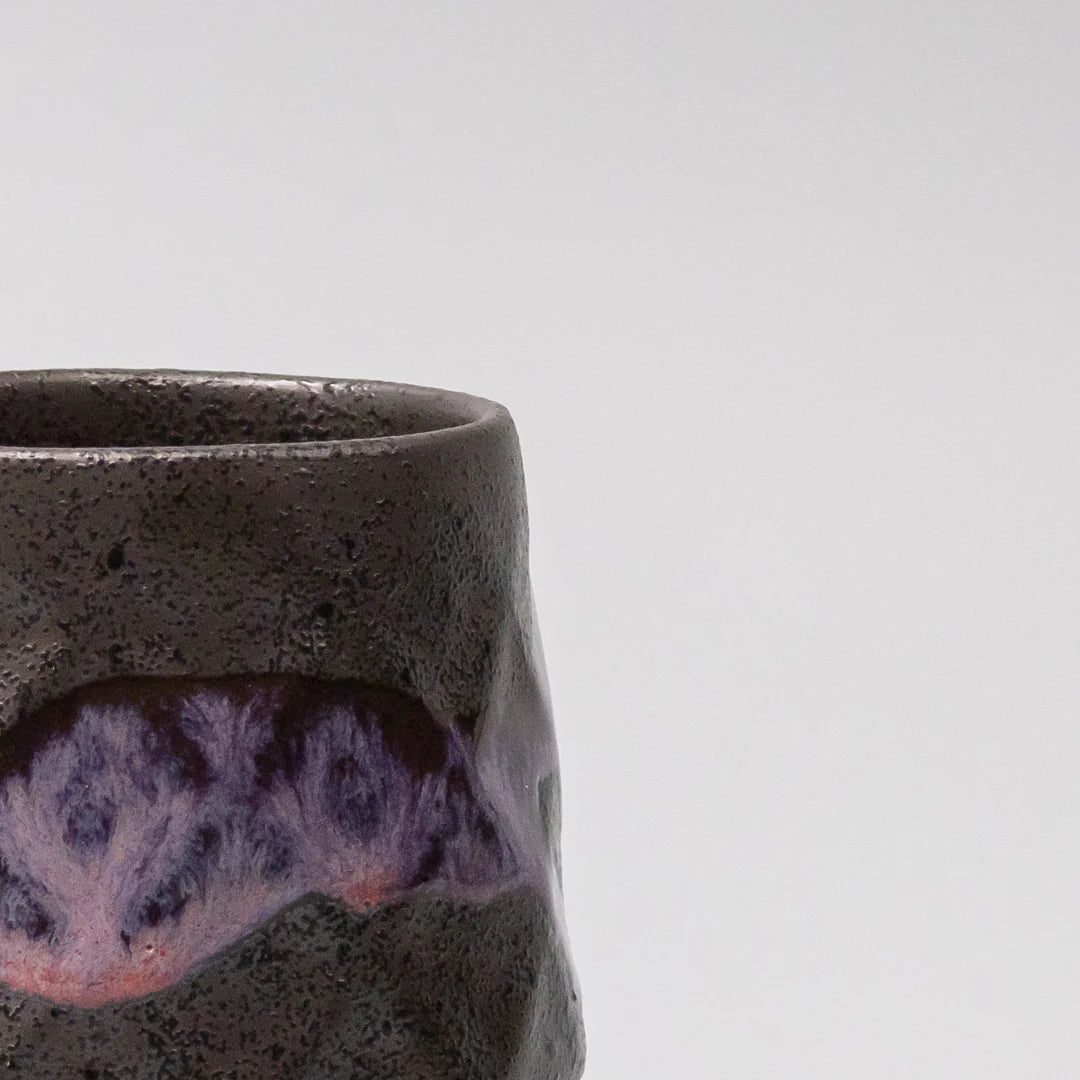 Close-up of a dark ceramic cup with purple interior on a light gray background
