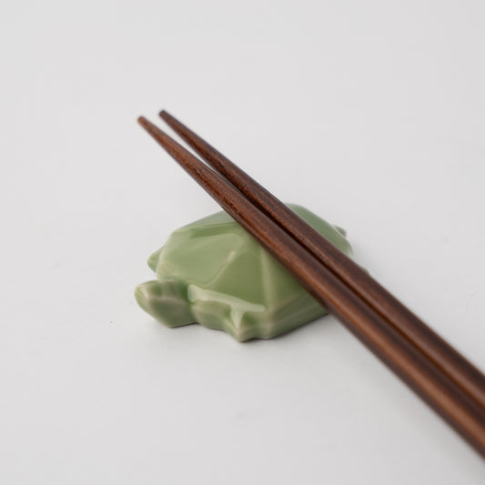 Green turtle-shaped chopstick rest with brown wooden chopsticks on a light gray background