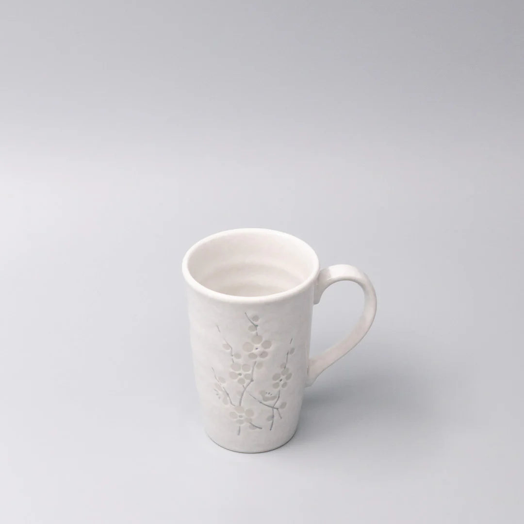 White ceramic mug with floral embossing on a light gray background