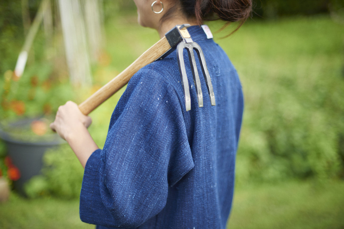 Person wearing a blue apron holding a garden fork with a blurred garden background